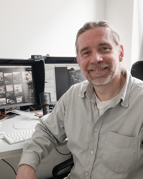 Karol Bagiński w koszuli, na tle komputerów.